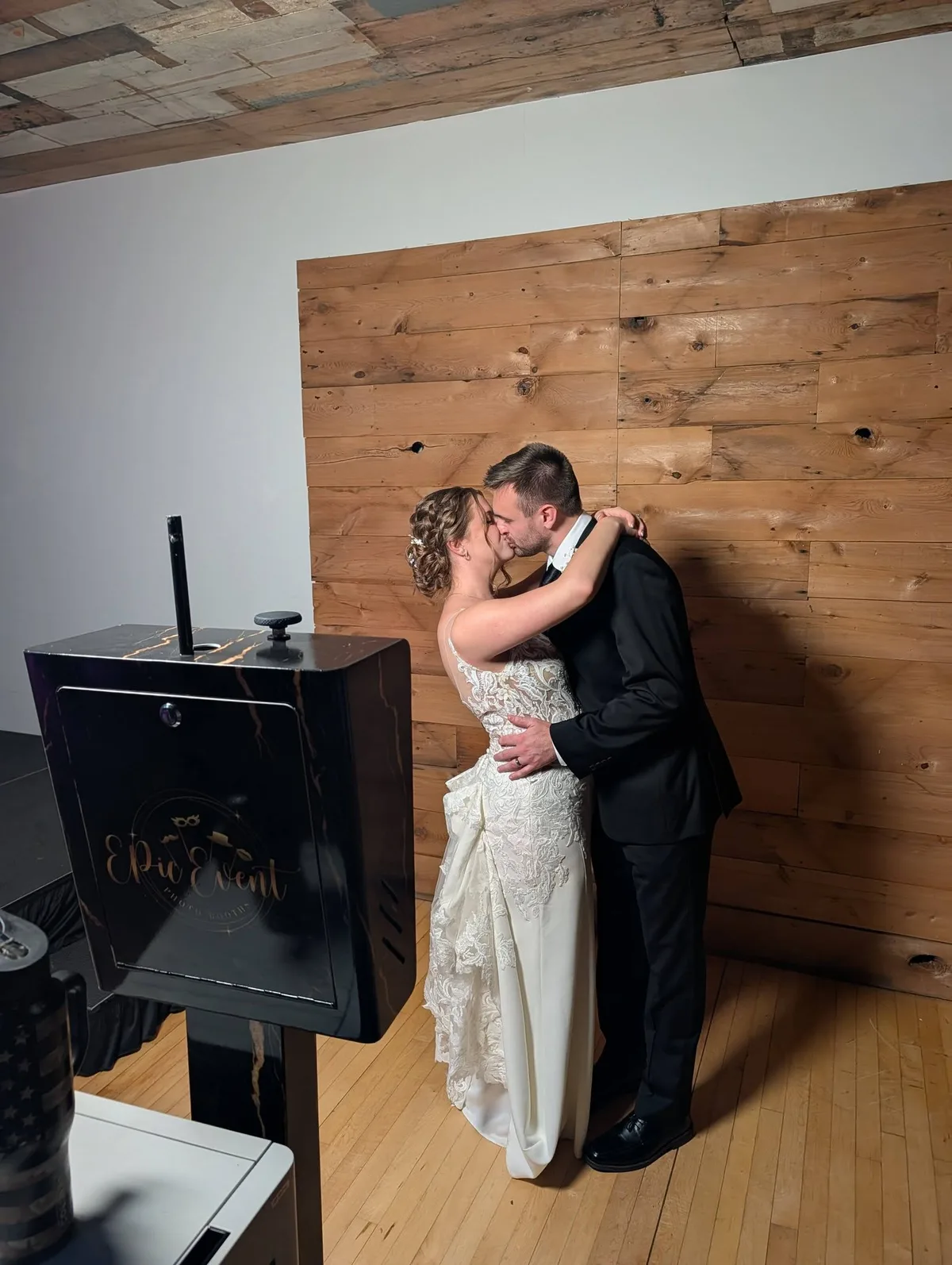 Bride and groom kissing in front of a wood-plank wall, the Onyx booth and its gold logo in the foreground